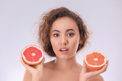 Beautiful young woman with acne problem holding grapefruit on light background. Skin allergy
