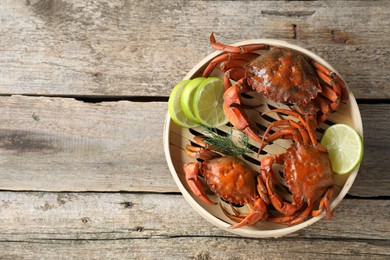 Photo of Delicious boiled crabs with lime and dill in bamboo steamer on wooden table, top view. Space for text