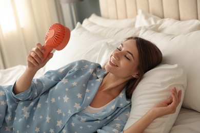 Photo of Woman enjoying air flow from portable on bed in room. Summer heat