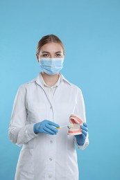 Photo of Dental assistant with jaws model and toothbrush on light blue background. Oral care demonstration