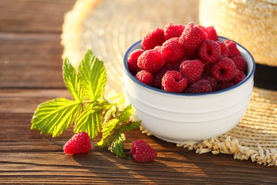 Photo of Tasty ripe raspberries, green leaves and straw hat on wooden table, closeup