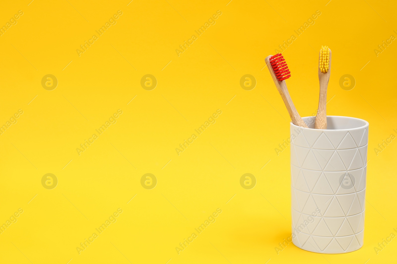 Photo of Toothbrushes made of bamboo in holder on yellow background. Space for text