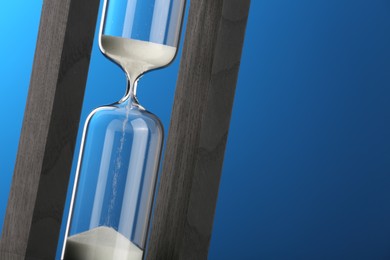 Photo of Hourglass with flowing sand on blue background, closeup. Space for text