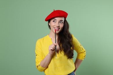 Photo of Woman with paintbrush on pale green background. Young artist