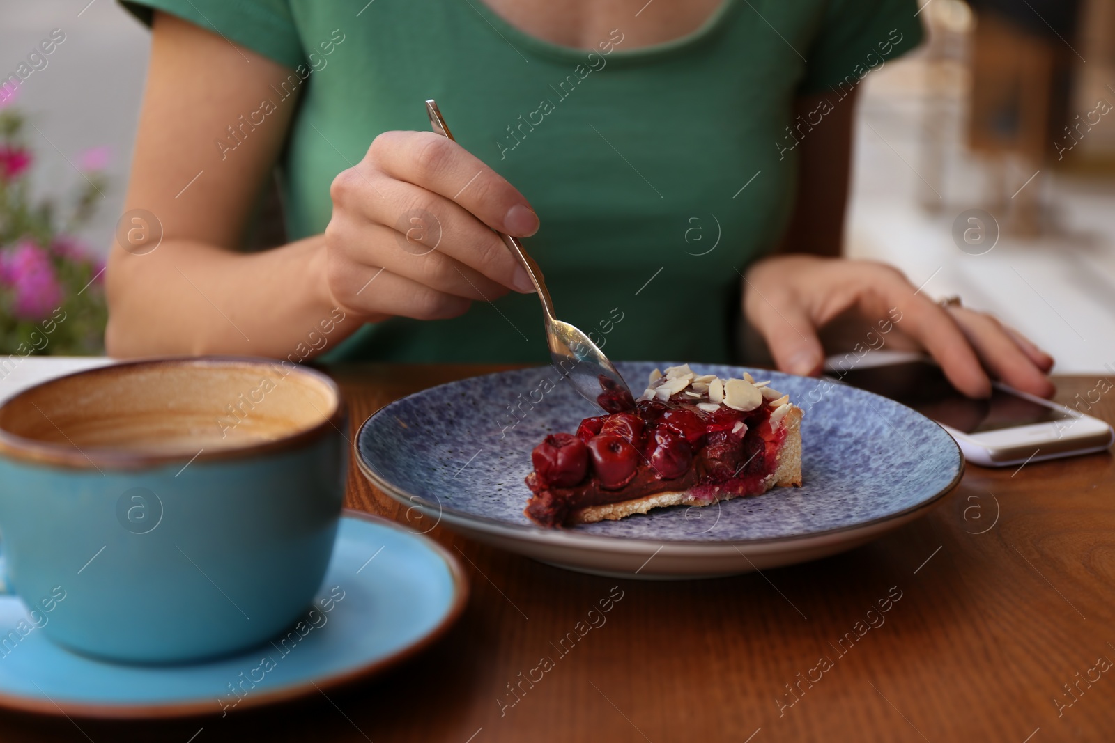 Photo of Woman eating slice of cherry cake at table, closeup