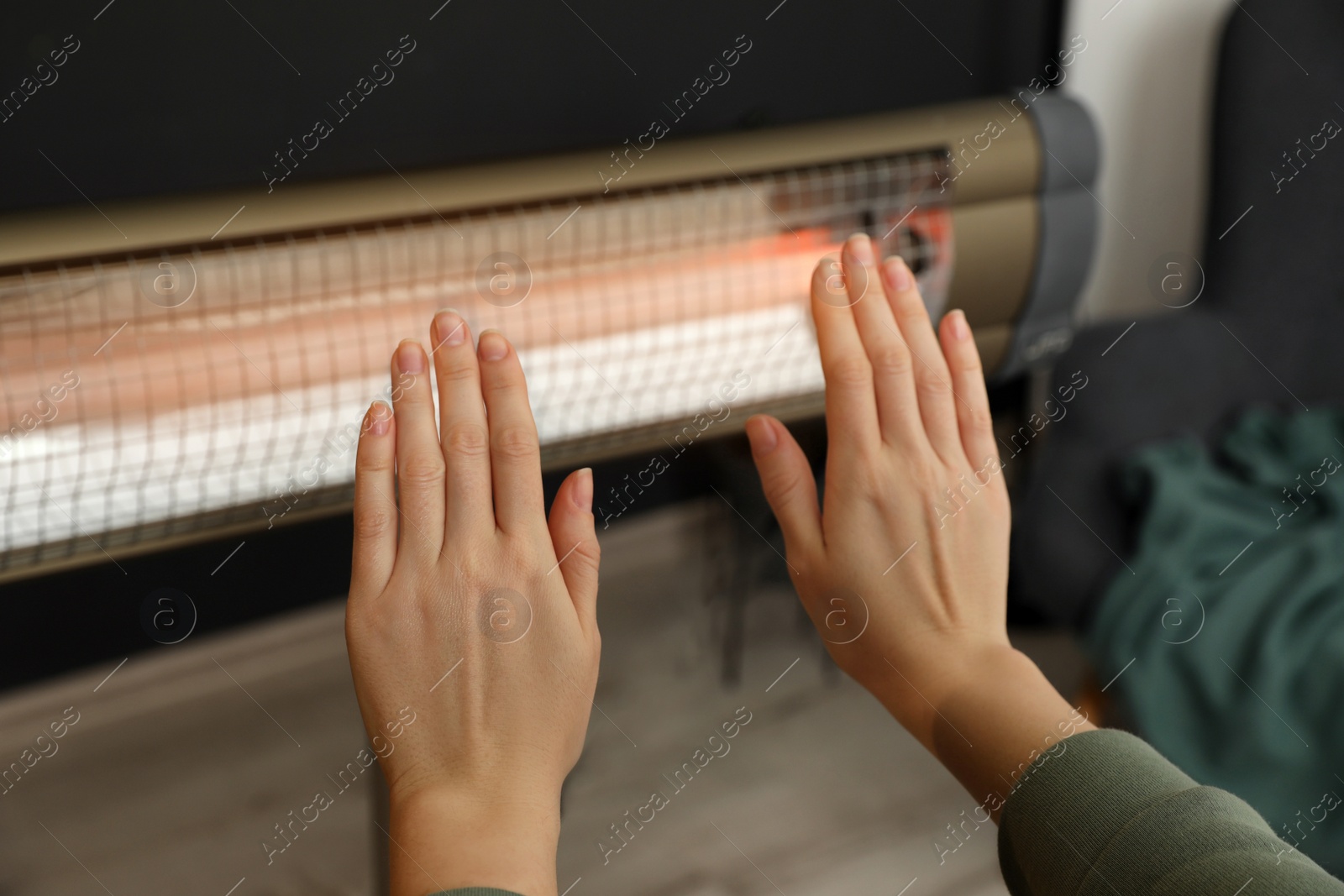Photo of Woman warming hands near electric infrared heater indoors, closeup