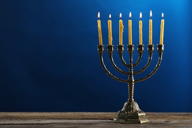 Photo of Hanukkah celebration. Menorah with burning candles on wooden table against blue background, space for text