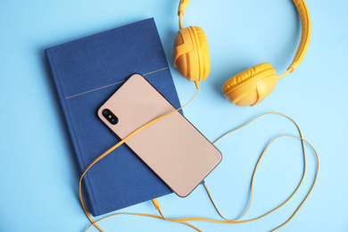 Photo of Book, modern headphones and smartphone on light blue background, flat lay