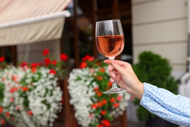 Photo of Woman holding glass of rose wine outdoors, closeup. Space for text