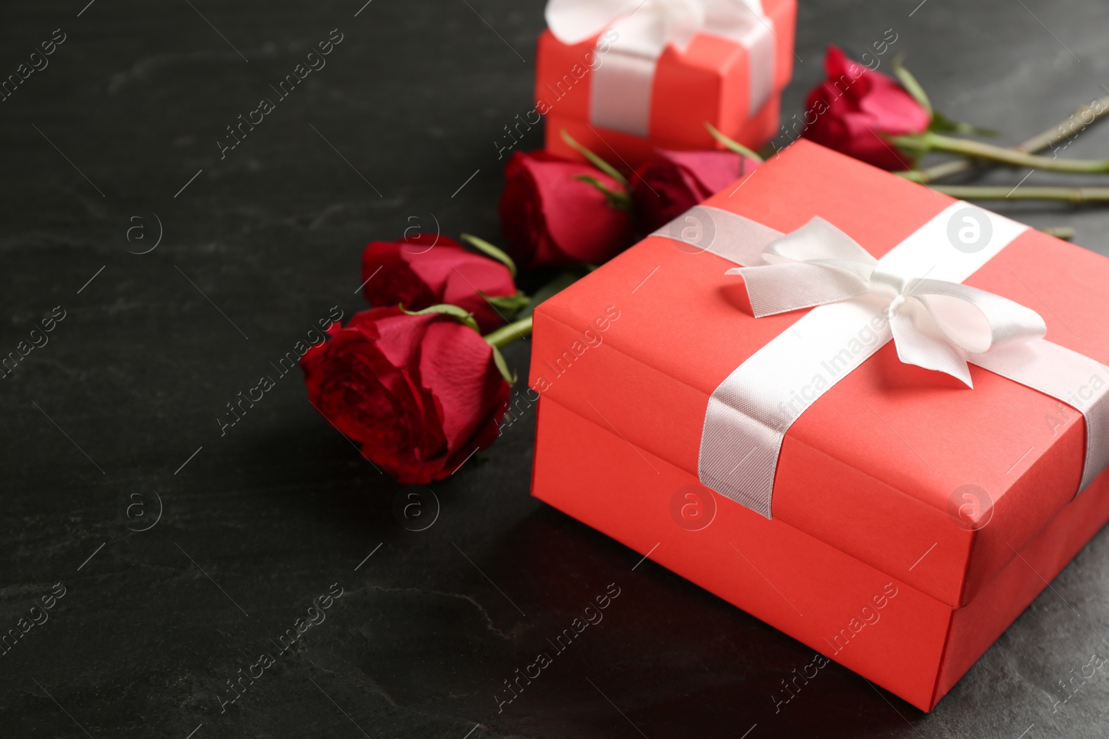 Photo of Beautiful gift box and roses on black table, space for text. Valentine's Day celebration