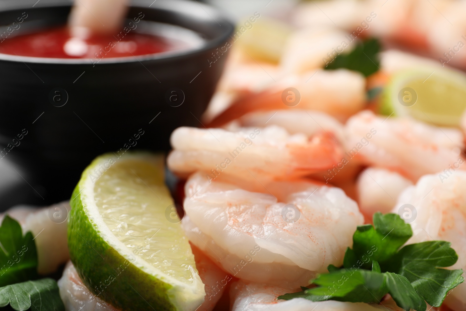 Photo of Tasty boiled shrimps with cocktail sauce, parsley and lime on plate, closeup
