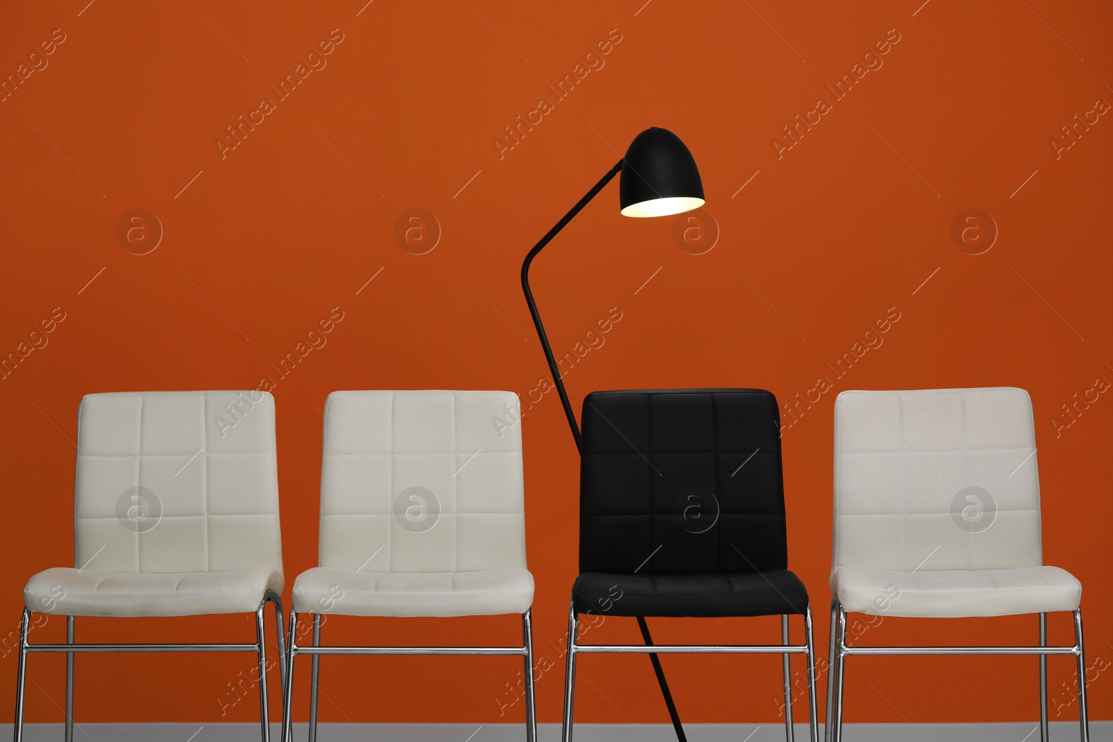 Photo of White chairs with black one and lamp near orange wall. Recruiter searching employee