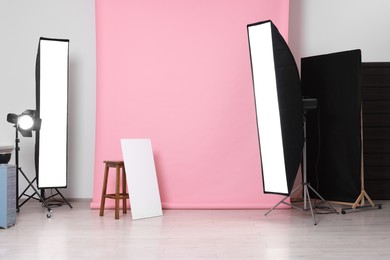 Photo of Pink photo background, stool and professional lighting equipment in studio