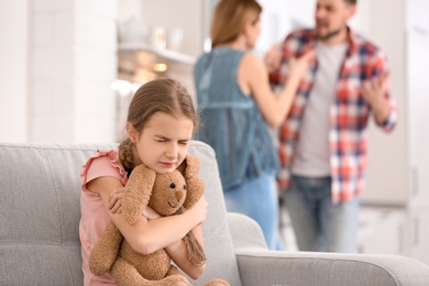 Little unhappy girl sitting on sofa while parents arguing at home