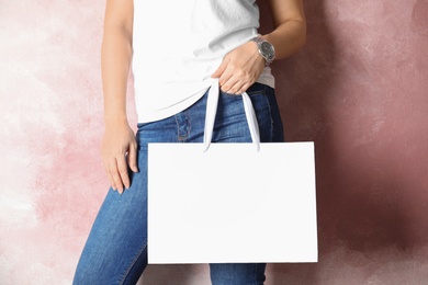 Woman holding mock-up of paper shopping bag on color background