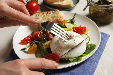 Photo of Woman eating delicious burrata salad at white wooden table, closeup