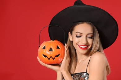 Photo of Beautiful woman wearing witch costume with Jack O'Lantern candy container on red background. Halloween party