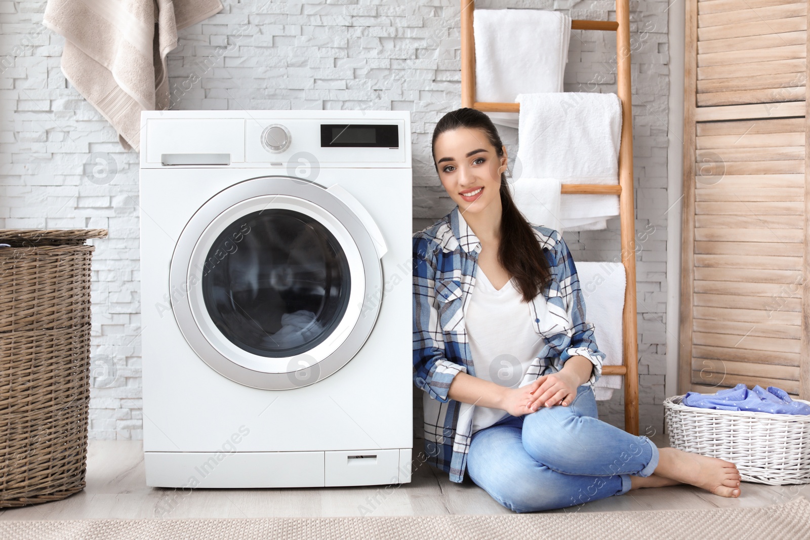 Photo of Young woman sitting near washing machine in laundry room