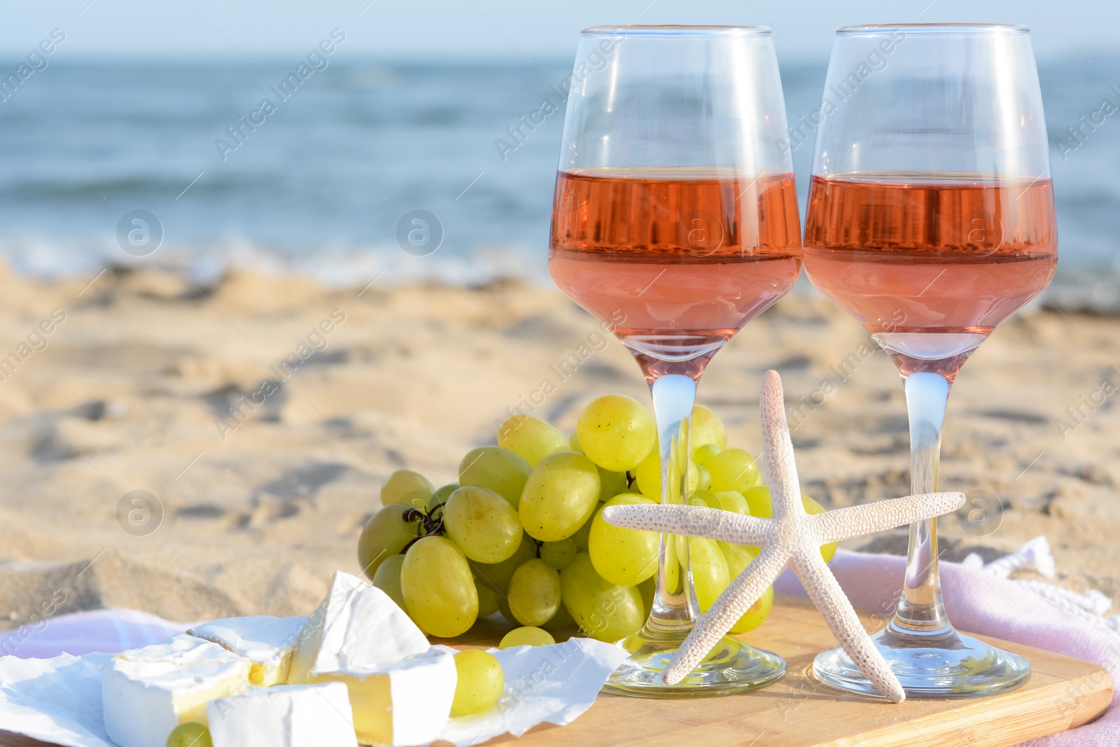 Photo of Glasses with rose wine and snacks on sandy seashore, closeup. Space for text