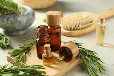 Photo of Essential oils in bottles and rosemary on light gray table, closeup