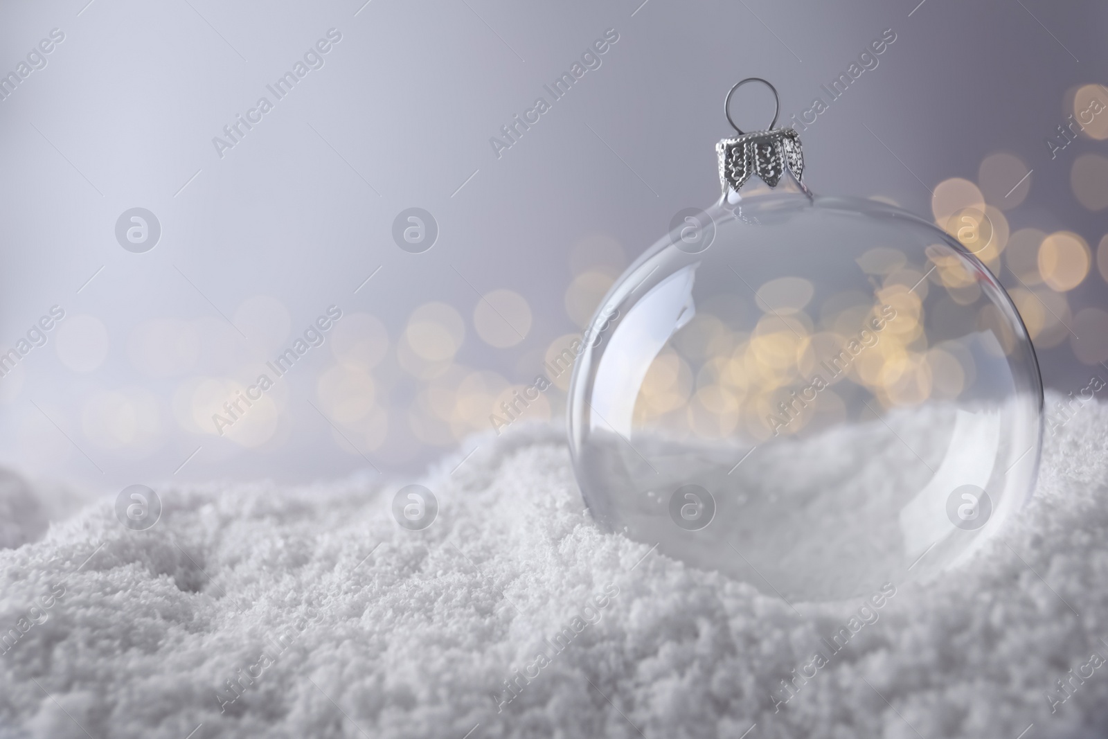 Photo of Transparent Christmas ball on snow against blurred fairy lights, space for text