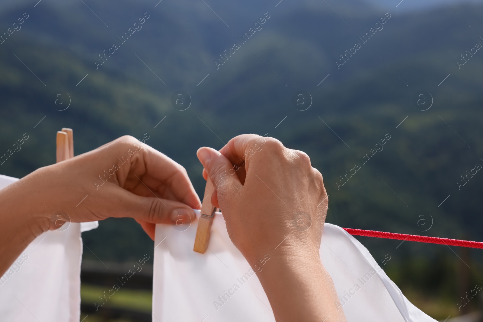 Photo of Woman hanging clean laundry with clothespins on washing line in mountains, closeup