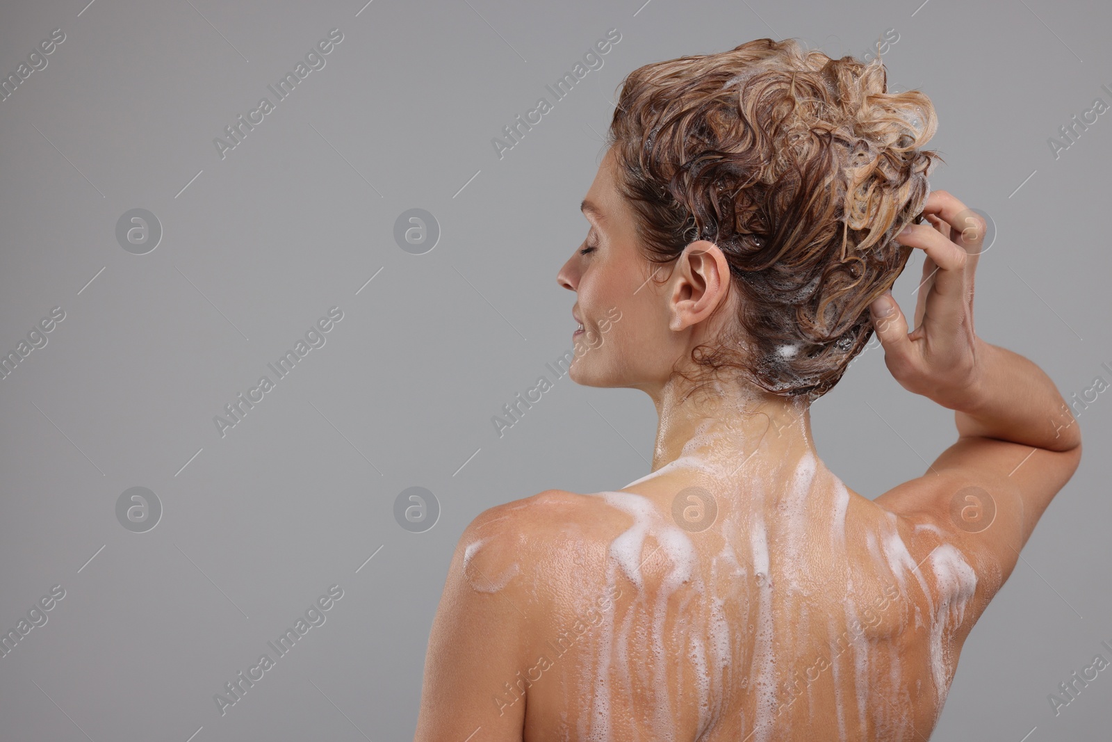 Photo of Woman washing hair on light grey background, back view. Space for text