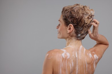 Woman washing hair on light grey background, back view. Space for text