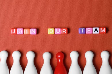Photo of Colorful cubes with phrase Join Our Team and pawns on red background, flat lay. Recruiter searching employee