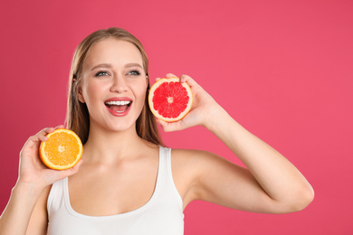 Photo of Emotional young woman with cut orange and grapefruit on pink background. Vitamin rich food