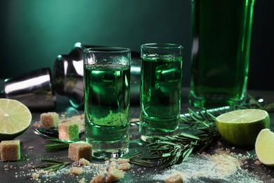 Absinthe in shot glasses, spoon, brown sugar, lime and rosemary on gray table, closeup. Alcoholic drink