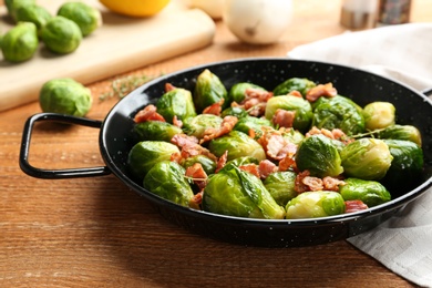 Tasty roasted Brussels sprouts with bacon on wooden table, closeup