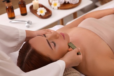 Young woman receiving facial massage with jade gua sha tool in beauty salon, closeup