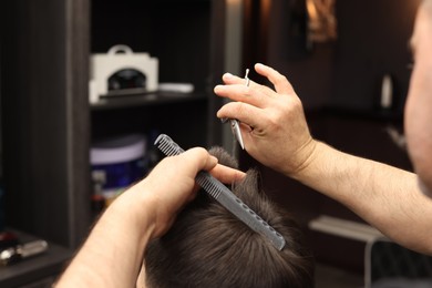 Photo of Professional hairdresser cutting man's hair in barbershop, closeup