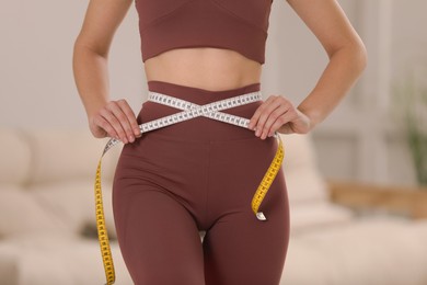 Photo of Woman in sportswear measuring waist with tape at home, closeup
