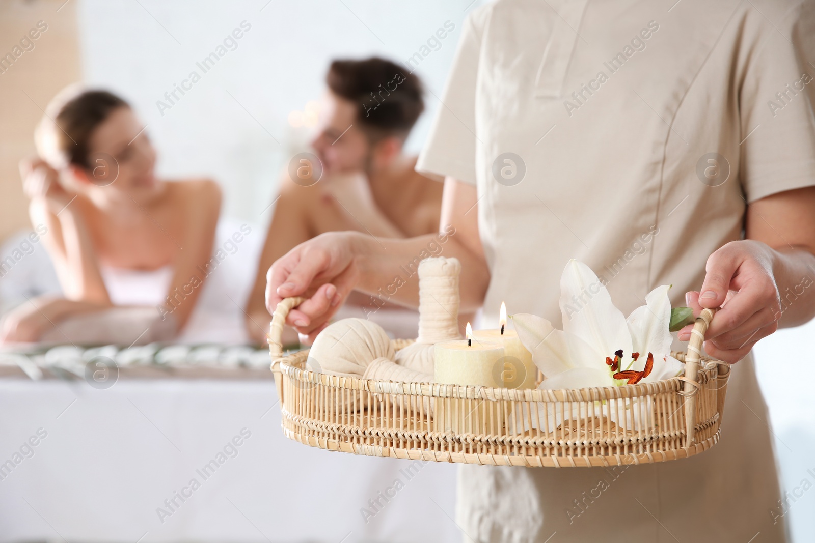 Photo of Massage therapist with spa essentials and young couple in wellness center