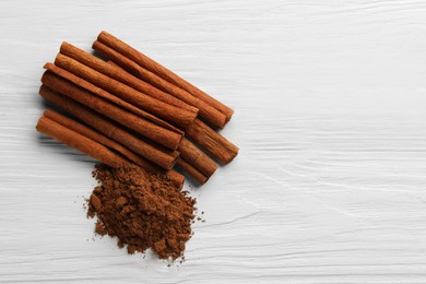 Dry aromatic cinnamon sticks and powder on white wooden table, top view. Space for text