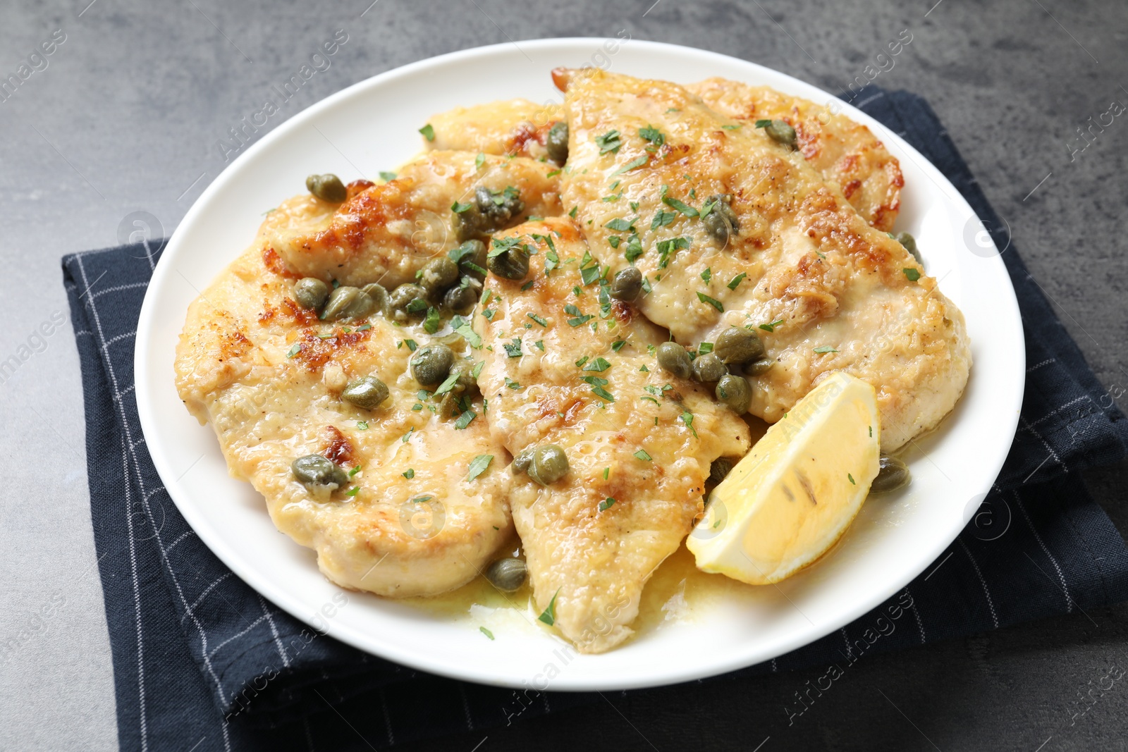 Photo of Delicious chicken piccata with herbs on grey table