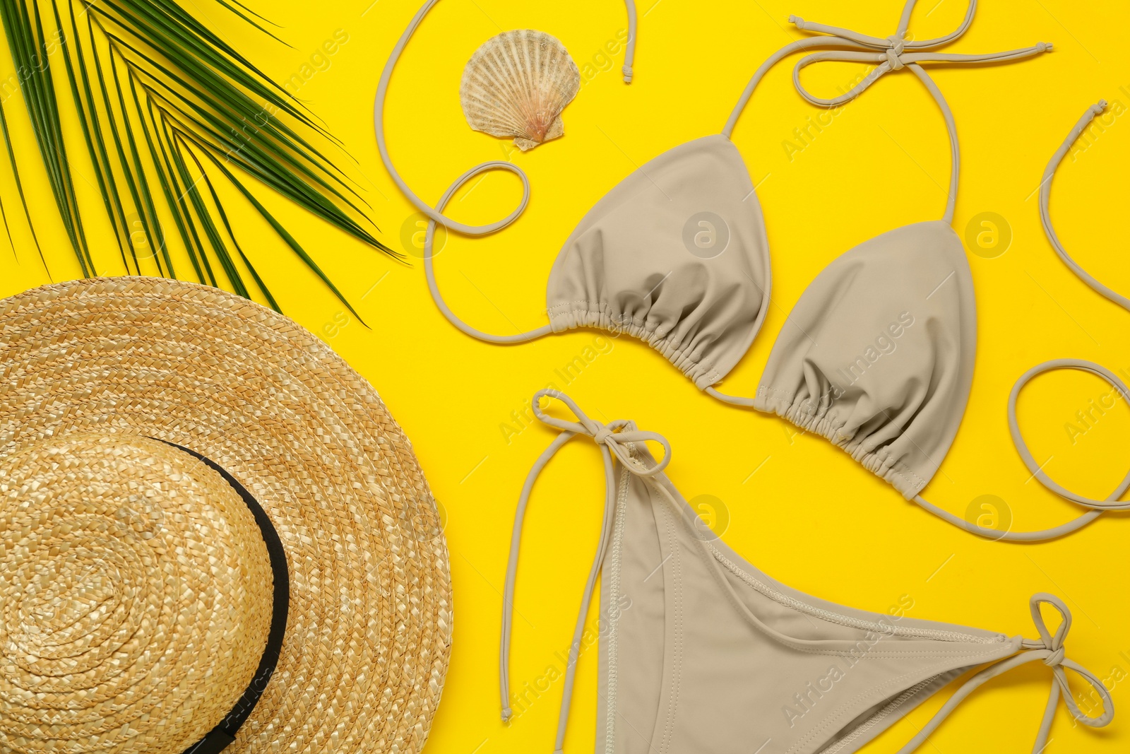 Photo of Stylish beige bikini, hat and seashell on yellow background, flat lay