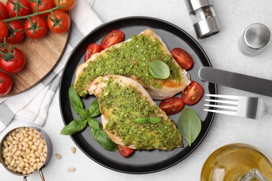 Delicious chicken breasts with pesto sauce, tomatoes and cutlery served on light gray table, flat lay