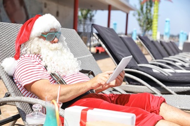 Authentic Santa Claus using tablet on lounge chair at resort