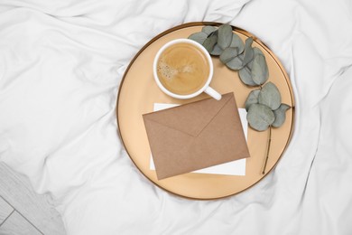 Photo of Tray with cup of coffee, envelope and eucalyptus branch on white bed, top view