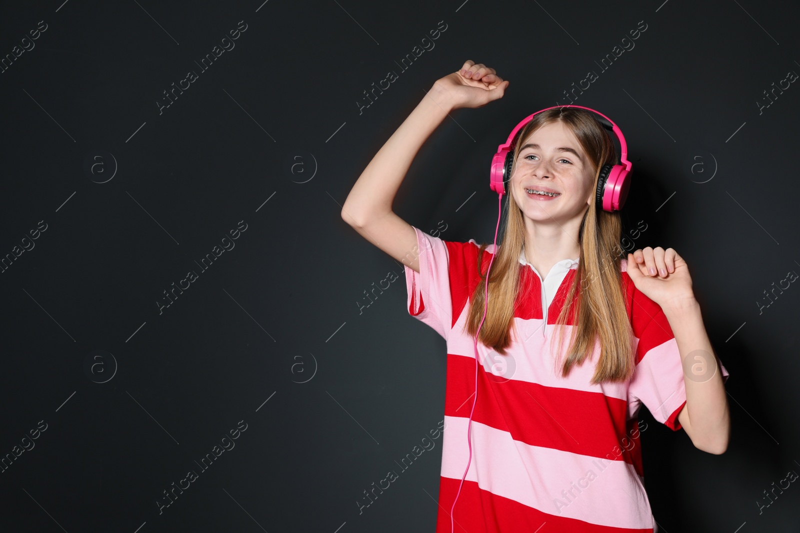 Photo of Teenage girl enjoying music in headphones on black background. Space for text