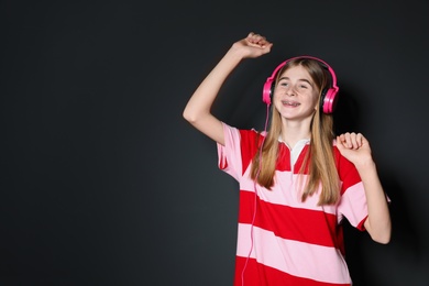 Photo of Teenage girl enjoying music in headphones on black background. Space for text