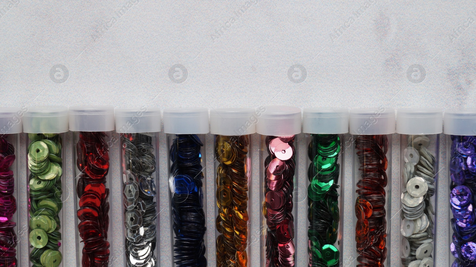 Photo of Many colorful sequins in containers on light grey background, top view. Space for text