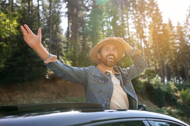 Photo of Enjoying trip. Happy man leaning out of car roof on sunny day