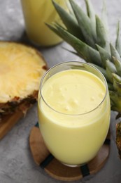 Photo of Tasty pineapple smoothie and fruit on grey table, closeup