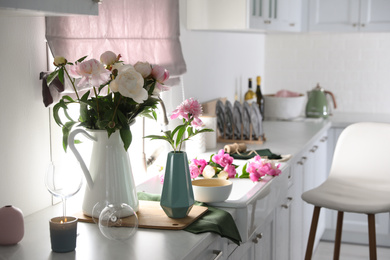 Photo of Beautiful peonies in vases on kitchen counter