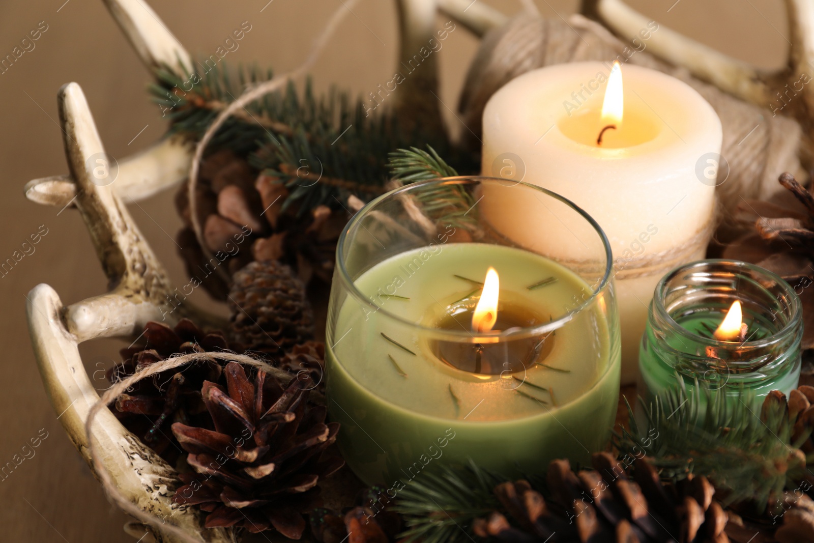 Photo of Burning scented conifer candles with Christmas decor on table, closeup