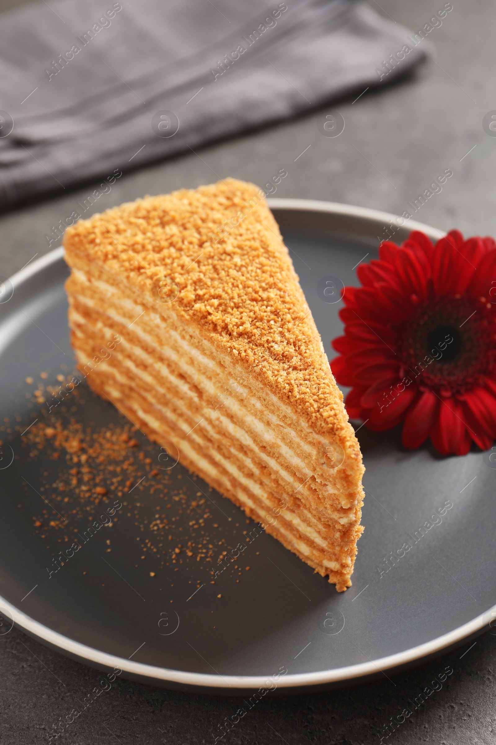 Photo of Slice of delicious layered honey cake served on grey table, closeup